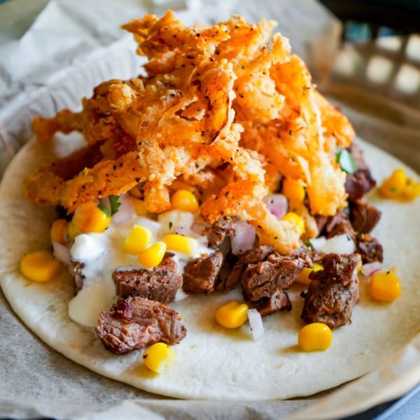 Crush Taco's beef taco with corn, onions, white sauce, and crispy fried toppings on a tortilla.