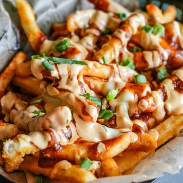Close-up of golden french fries topped with creamy sauce, red drizzle, and green onions.