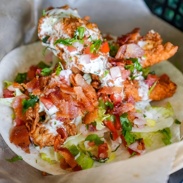 Close-up of a Crush Taco with crispy fried chicken, bacon, lettuce, tomato, and white sauce.