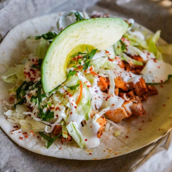 A Crush Taco chicken taco with avocado, lettuce, and white sauce on a tortilla.